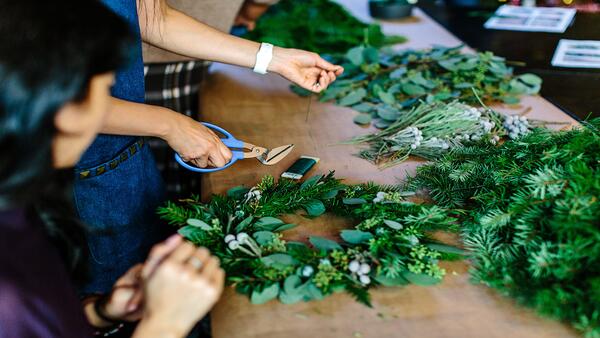 close up of two people working handling greenery to make a wreath