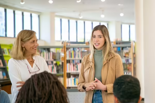 girl speaking to others in a library with instructor listening