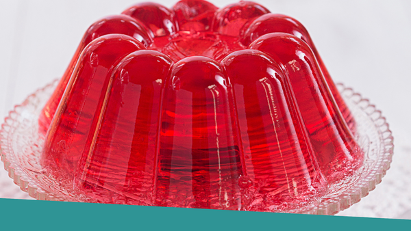 A red jello mold sitting on top of a glass cake plate.