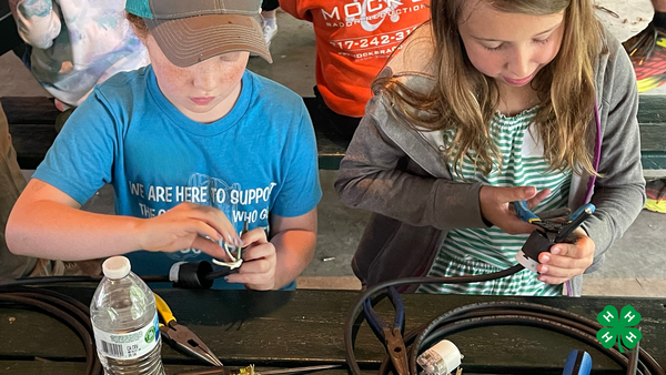 two 4-H members sit at a table with tools and electrical cords, connecting and creating extension cords.