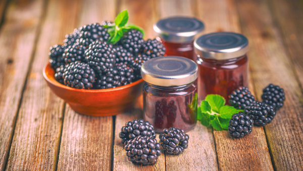 Bowl of blackberries next to jars of jam