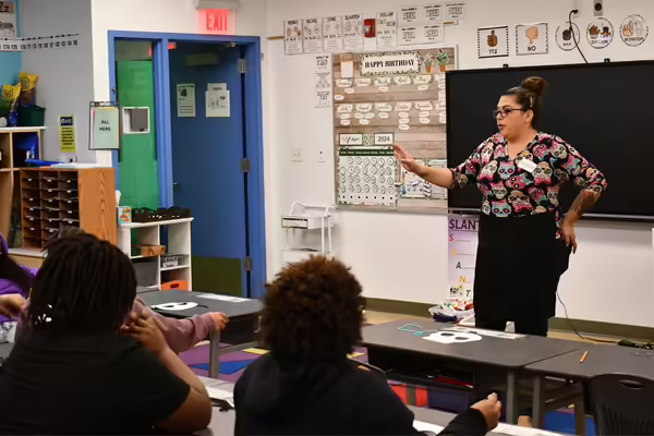 A woman in a colorful shirt stands at the front of a classroom.