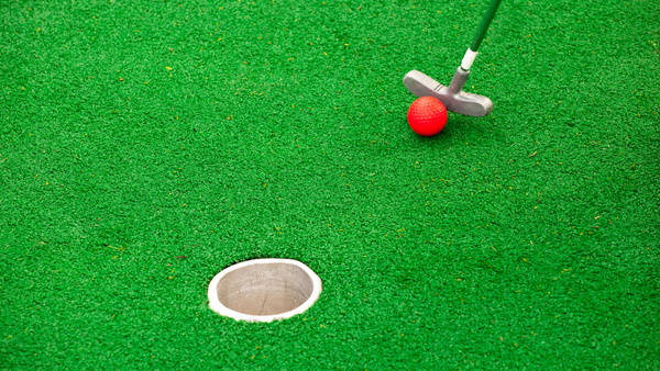 A mini golf course hole is present with a club and a ball.