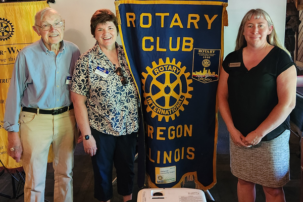 man and two woman standing next to Rotary Club Oregon IL flag