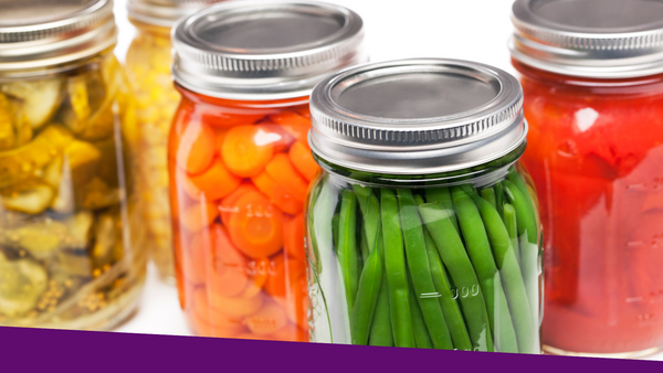 Vegetables in glass jars that are pickled or sliced, including carrots, green beans, corn, cucumbers, and tomatoes.