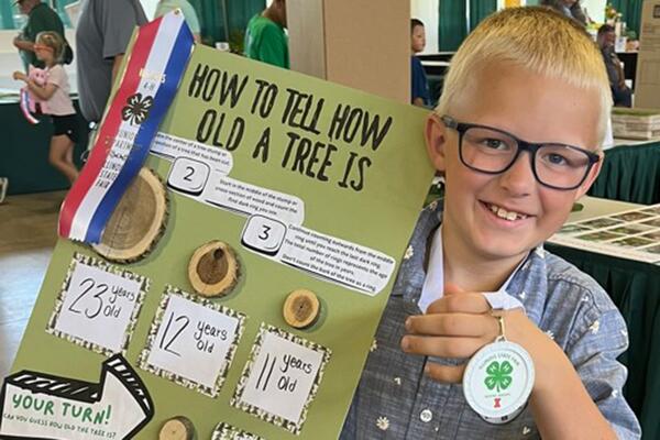 4-H member holding a poster about trees and wearing a white medallion