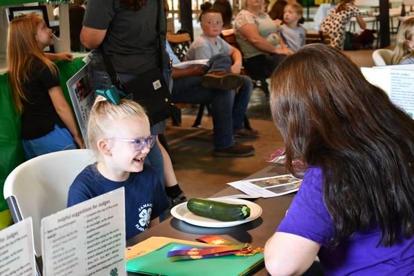 A smiling child talking to an adult about their fair project.