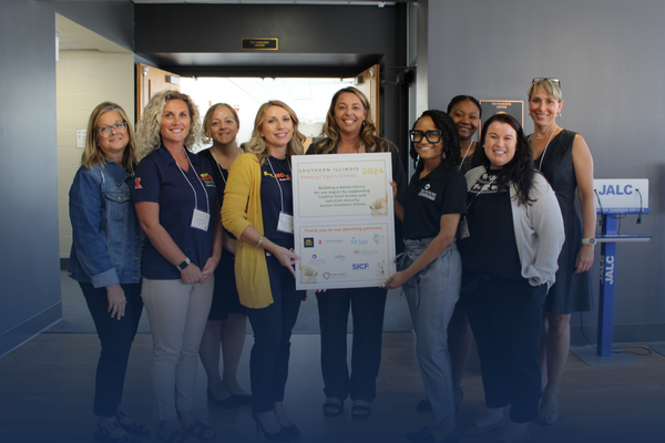 Group photo of female educators and professionals holding a sign and smiling at the camera