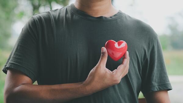 Male presenting body holding a heart shape in front of their chest