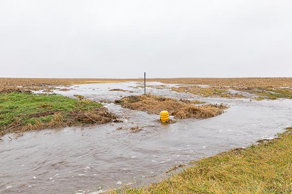 Water flooding and rushing through a drainage system in a farm field.