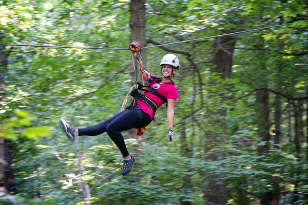 woman on zip line in pink shirt going through woods