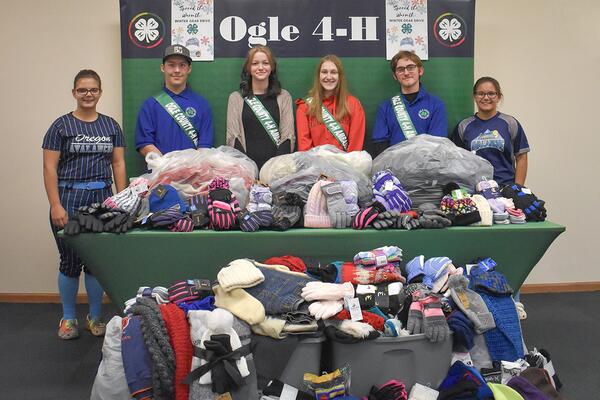 Six youth standing behind bags and bins of clothing.