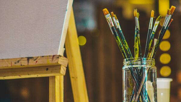 paintbrushes in a jar sitting next to a blank canvas