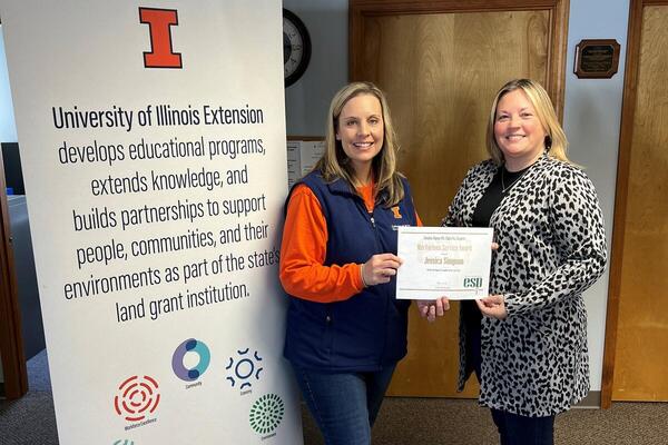 Tara Buerster presenting award to Jessica Simpson with Extension banner in background