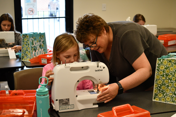 A volunteer helps a young girl operate her sewing machine.