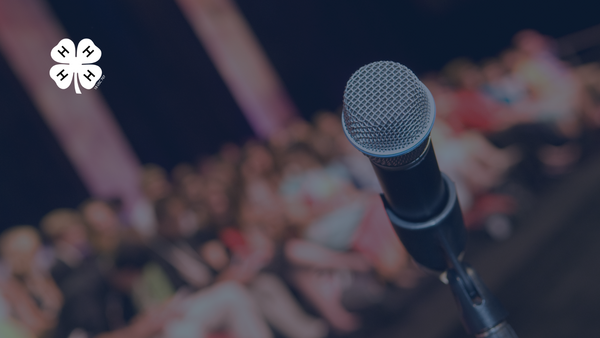 A microphone on a microphone stand. A white 4-H clover in the top left corner.