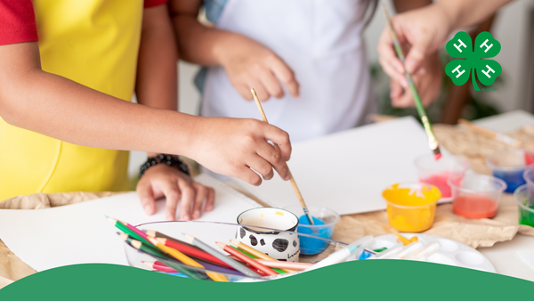 Youth holding paint brushes getting ready to paint on a piece of paper. Paint and brushes are sitting on the table.