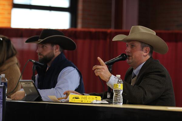 Two people sitting behind a table taking notes and bids at an auction.