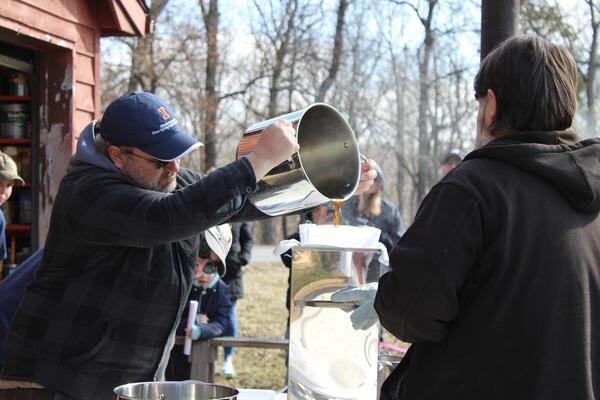 A man pours sap from a metal pot to another container outside