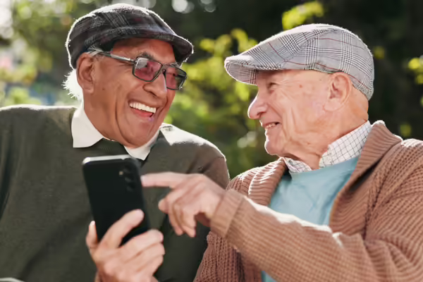 Two elderly men sharing an electronic device and laughing