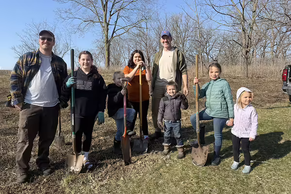 Group of adults and youth standing with shovels on grass