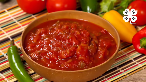 A bowl of salsa of sitting on a placemat with peppers and tomatoes around the bowl.