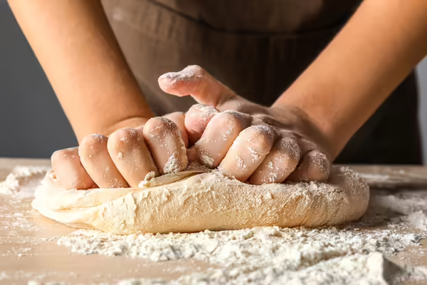 Two hands kneading bread dough on a cutting board with flour