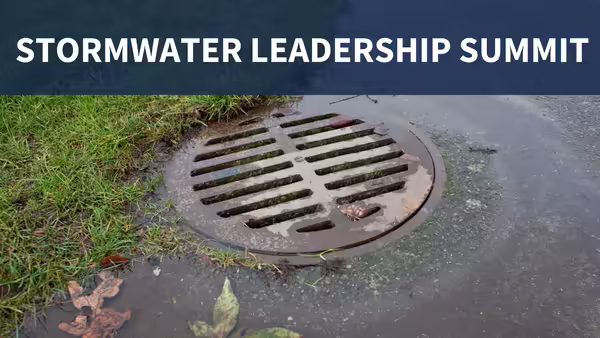 A close-up image of a circular storm drain grate surrounded by grass, pavement, and fallen leaves, with "STORMWATER LEADERSHIP SUMMIT" text displayed across the top of the image on a dark blue overlay.