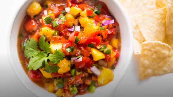 A white bowl with peach salsa in it with tortilla chips next to the side of the bowl.