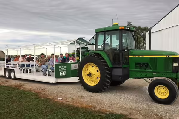 A green tractor pulls a seated trailer full of people around a farm tour