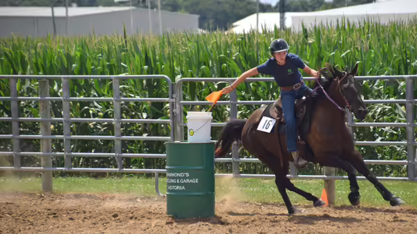a girl on a horse riding around a barrel