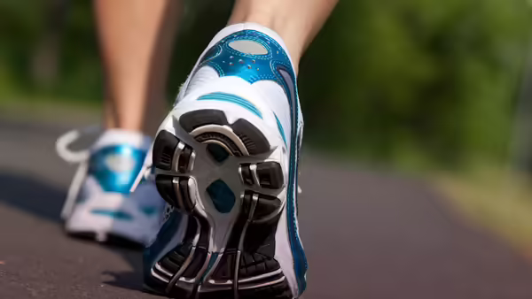 The sole of a person's tennis shoe as they walk on a paved surface.