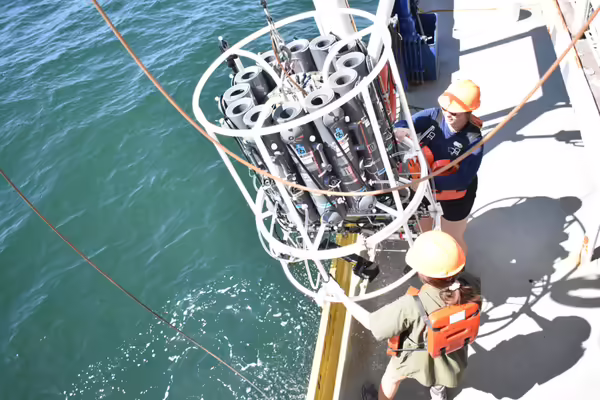People in hard hats handle equipment on the edge of a boat