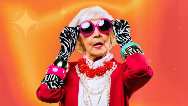 Older woman wearing pink sunglasses and a red blazer in front of an orange and red background that has faint twinkling stars