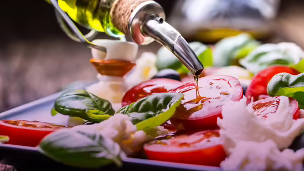 olive oil pouring on tomatoes, mozzarella, and basils