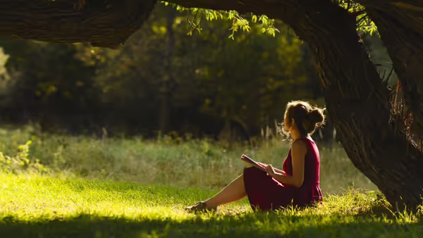 lady sitting on the ground under a tree holding a book
