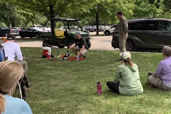 A group of people watch a training on using tools outdoors