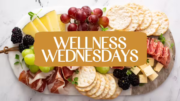Charcuterie board with fruit, cheese, and crackers overlaid with the text ‘Wellness Wednesdays’ in white on a gold background banner.