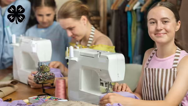 Youth working at sewing machines. A black 4-H clover in the upper left corner.