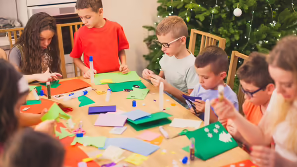 young kids working on crafts at a table with a holiday tree in the background