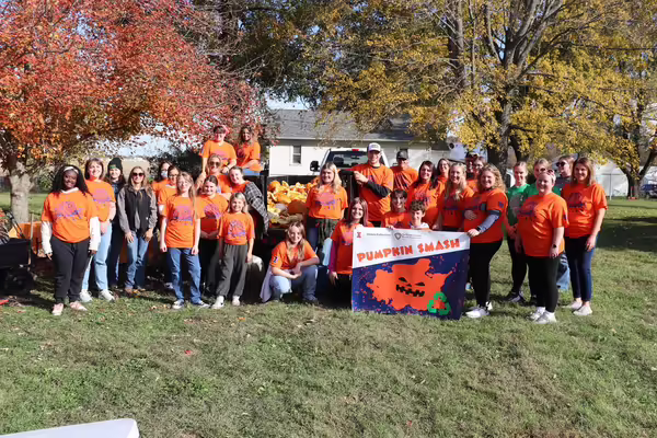 A group of people of different ages, shapes, and ethnicities together posing in front of a trailer of smashed pumpkins.