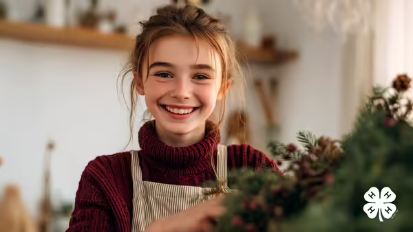 A girl holding holiday greenery. The white 4-H logo is in the bottom right corner.