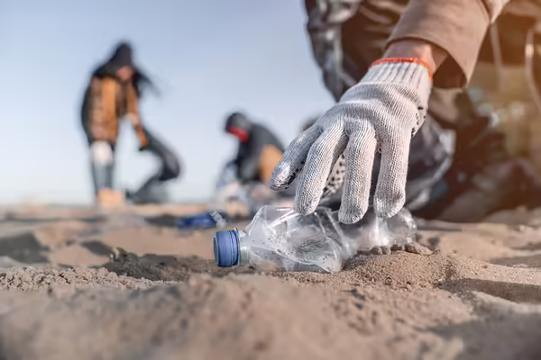 gloved hand picks up a plastic bottle on a beach