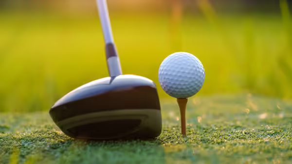 Golf ball sitting on a golf tee with a driver sitting next to it.