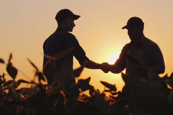 Two farmers talk on the field, then shake hands.