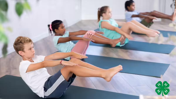 A group of kids doing a yoga pose on yoga mats. A green 4-H clover is in the bottom right corner.