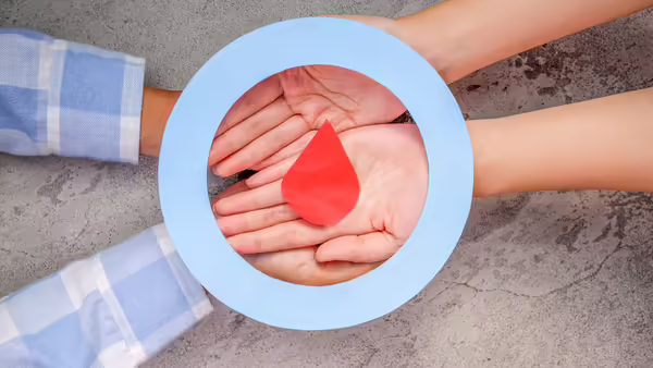 Hands gathered in a circle holding a red blood drop symbol.