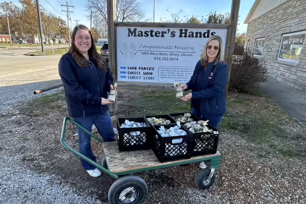 Extension staff holding packages of ground venison next to a cart with crates of venison and a local food pantry sign