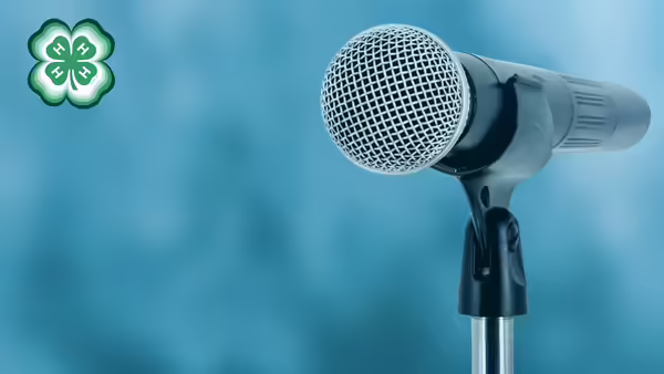 A microphone with a blue background. A green 4-H clover in the upper left corner.