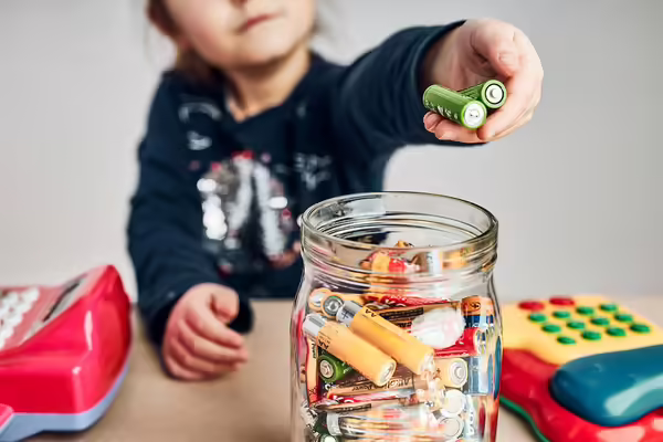 A child puts batteries into a glass container with other batteries